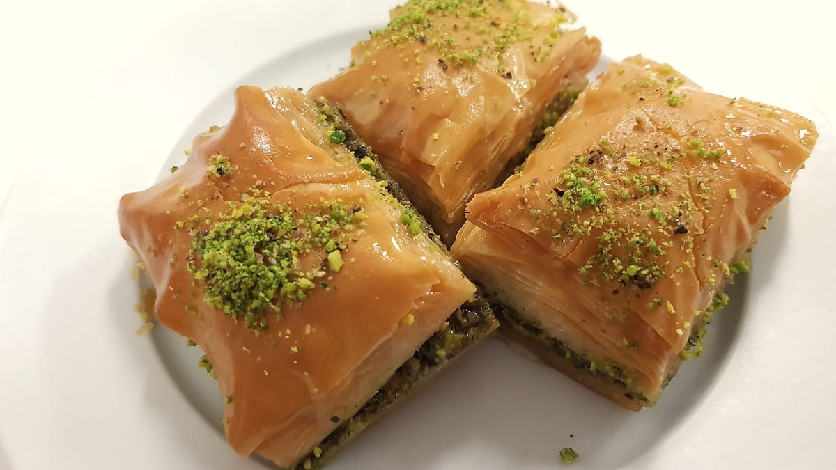Drei goldene Baklava-Stücke mit gehackten Pistazien auf einem Teller
