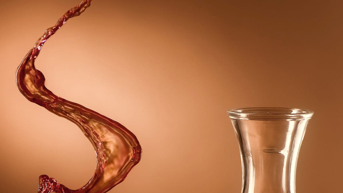 Rotwein spritzt schwungvoll aus einem Glas vor warmem Hintergrund