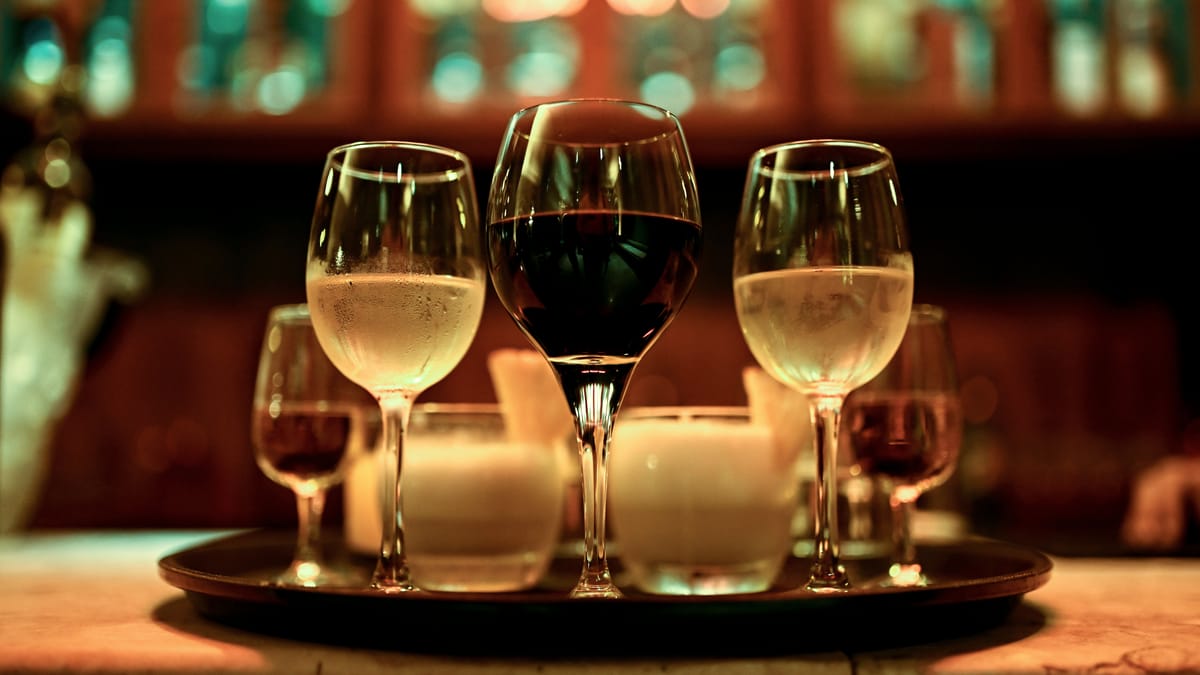 Zwei Gläser Weißwein und ein Glas Rotwein nebeneinander auf einem Tablett im warmen Kerzenlicht