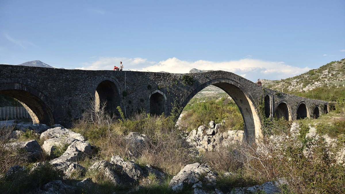 Die osmanische Mesi-Brücke (Ura e Mesit) bei Shkodra mit ihren Steinbögen vor Bergen und blauem Himmel